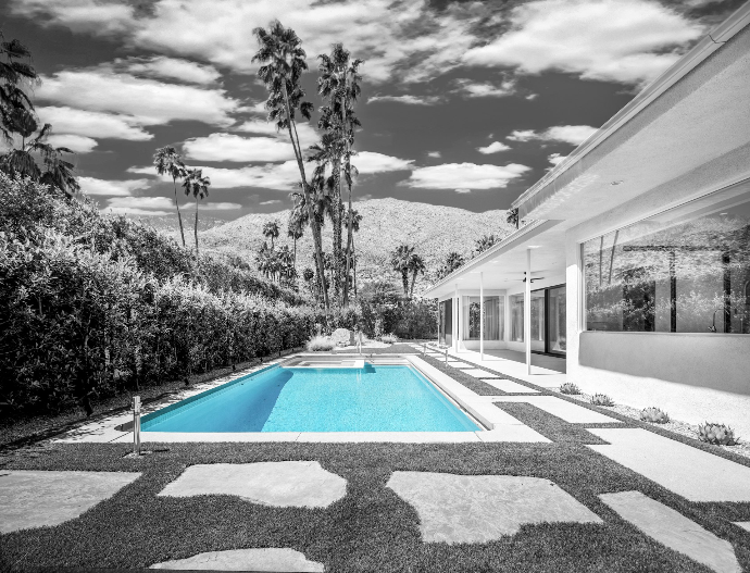 A bright blue swimming pool beside a modern house with palm trees and mountains